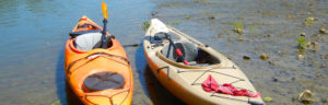 Photo of orange and tan colored kayaks in a shallow part of the river