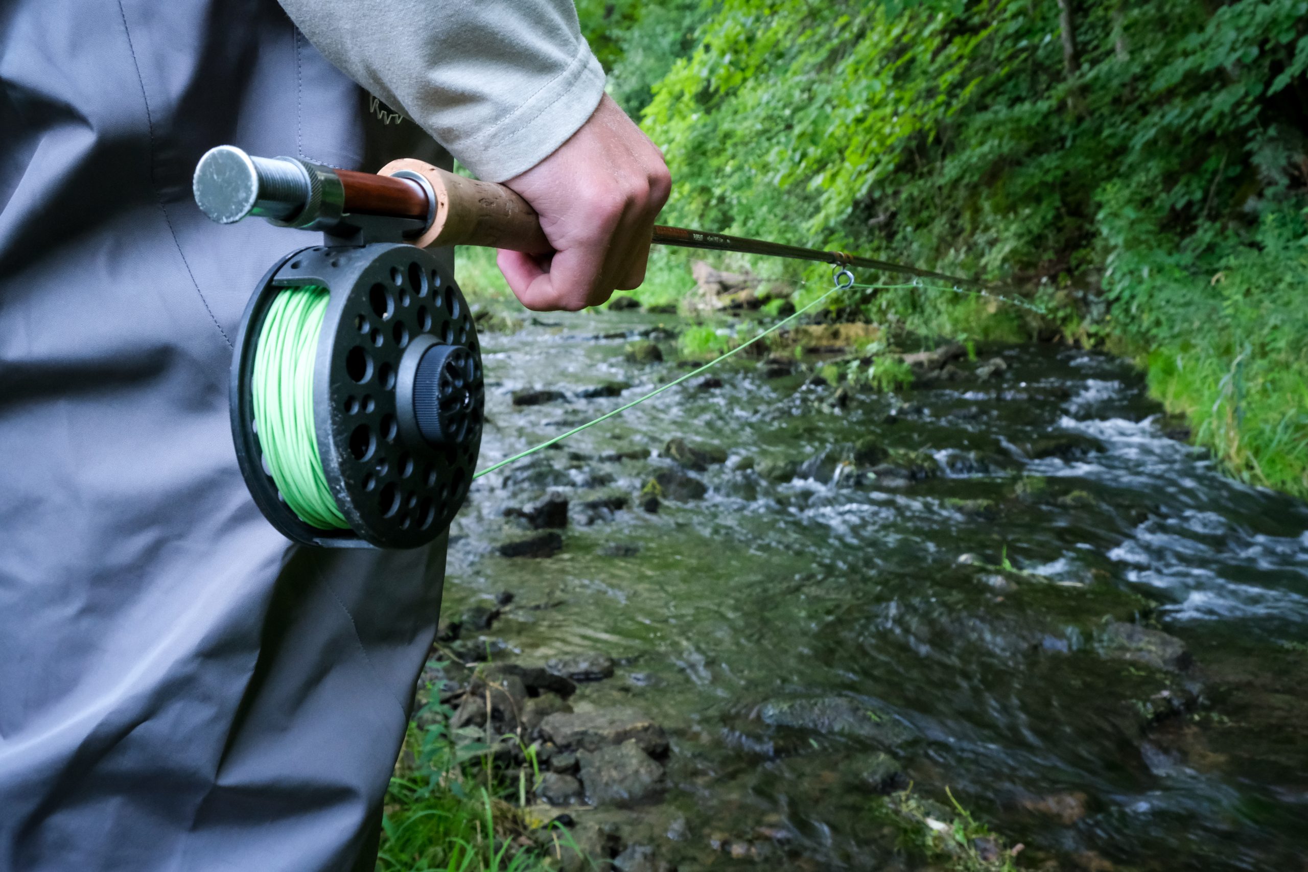 Man holding fly fishing rod in a cold water stream.