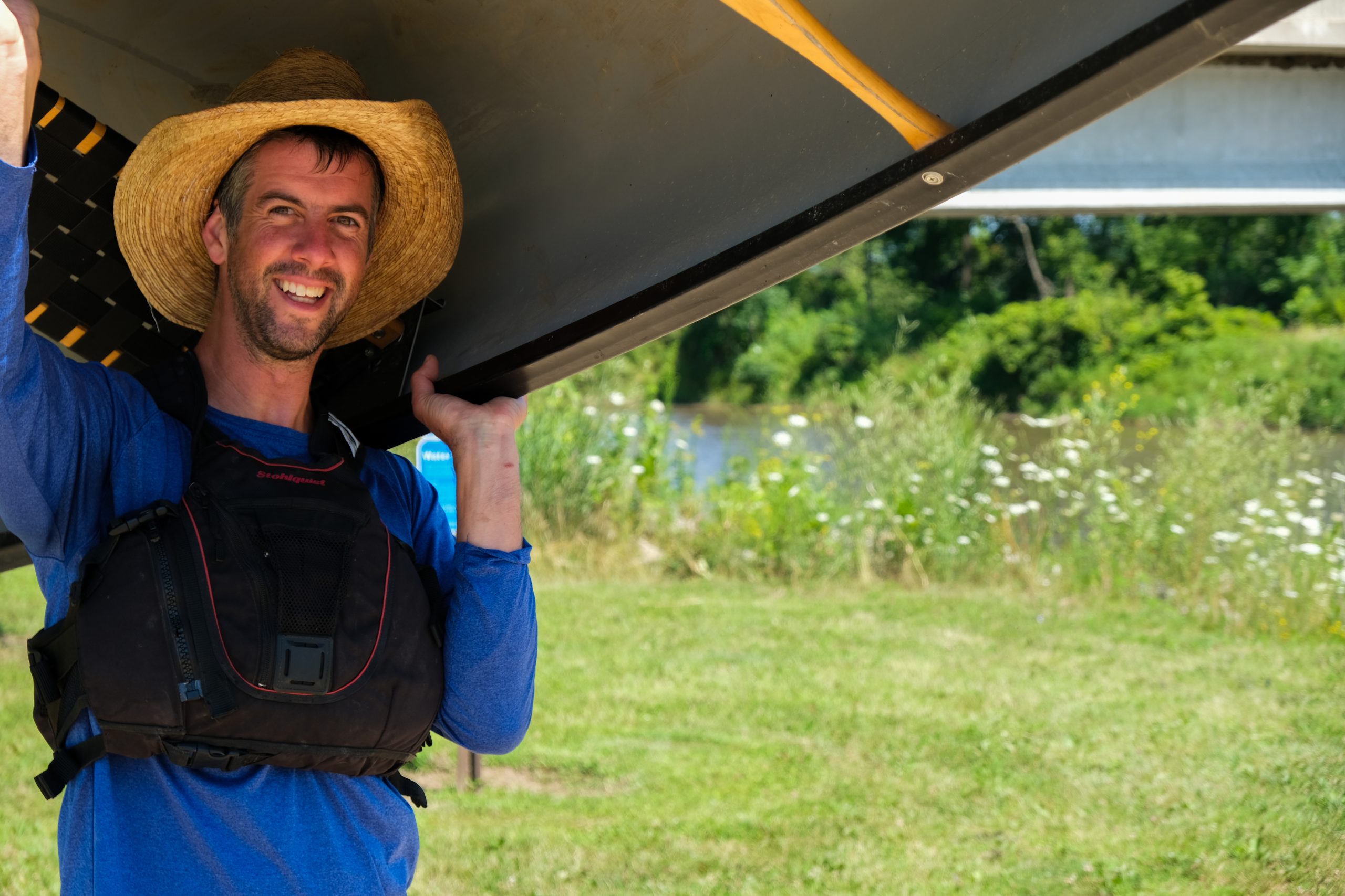 Man smiling and holding a canoe next to a water access.